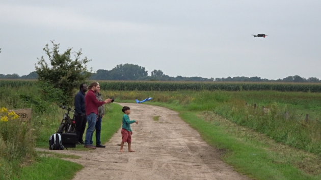 Three men and a young boy standing next to a field, flying a drone