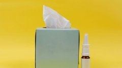 A box of tissues and nasal spray to a yellow background